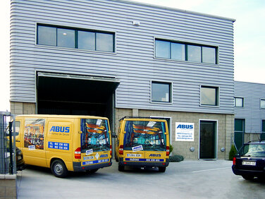 Edificio de la empresa ABUS Sistemas de Gruas en España Vista del moderno edificio de la empresa ABUS Sistemas de Gruas en España con apariencia metálica, con autobuses de servicio ABUS amarillos delante